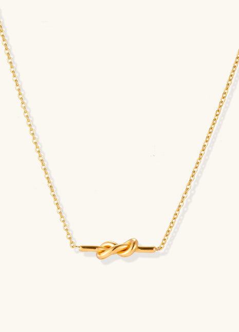 Dainty 18K gold plated stainless steel chain necklace with minimalist knot pendant on cream background.