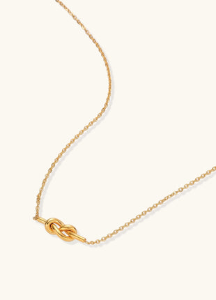 Dainty 18K gold plated stainless steel chain necklace with minimalist knot pendant on cream background.