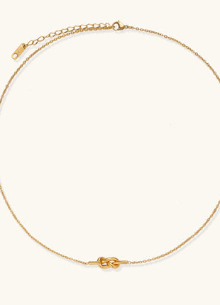 Dainty 18K gold plated stainless steel chain necklace with minimalist knot pendant on cream background.