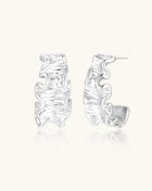 Textured gold-plated hoop earrings with flowing ripple design displayed on clean white background.