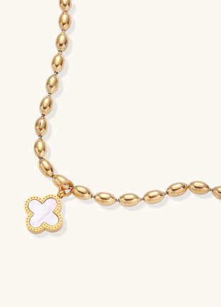 Dainty gold-plated beaded bracelet with oval links and four-leaf clover charm pendant on neutral background.