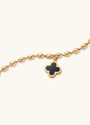 Dainty gold-plated beaded bracelet with oval links and four-leaf clover charm pendant on neutral background.