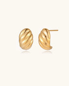 Pair of gold-plated twisted stud earrings with sculptural spiral design displaying elegant curved ridges on cream background.