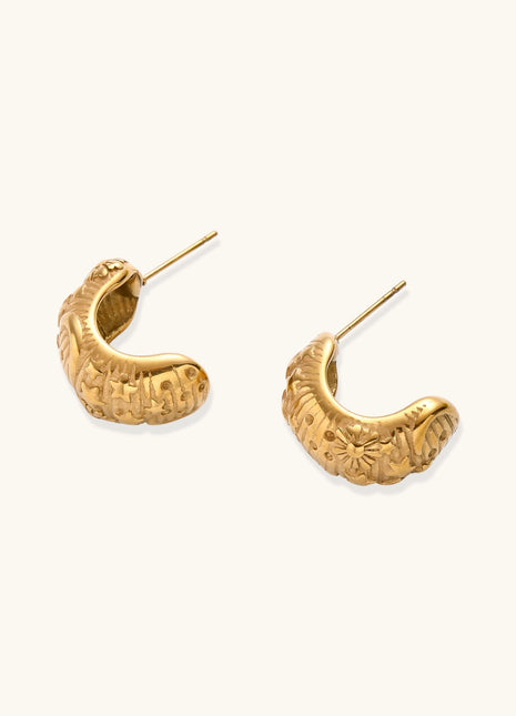 Close-up of ornate 14K gold-plated hoop earrings featuring embossed sun and star celestial motifs on neutral background.