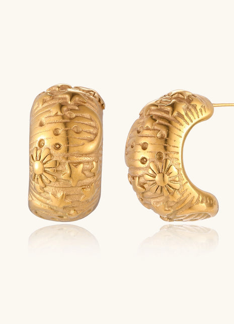 Close-up of ornate 14K gold-plated hoop earrings featuring embossed sun and star celestial motifs on neutral background.